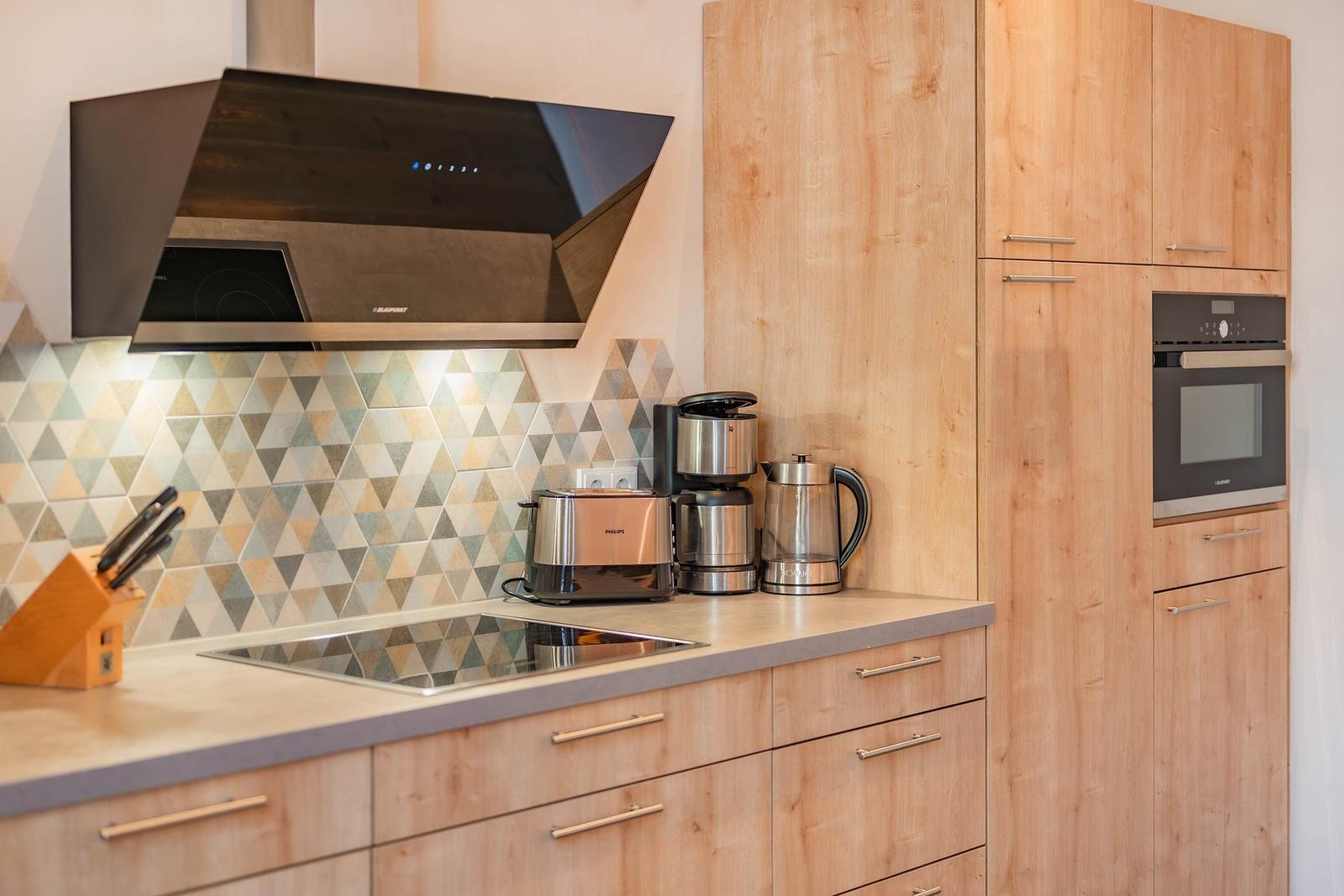 Moderne Küche mit Holzschränken, Edelstahlgeräten und Dreiecksfliesen an der Wand.