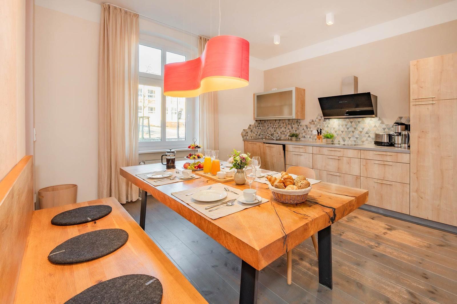 Essbereich mit Holztisch, Bänken und Küchenzeile im Hintergrund.