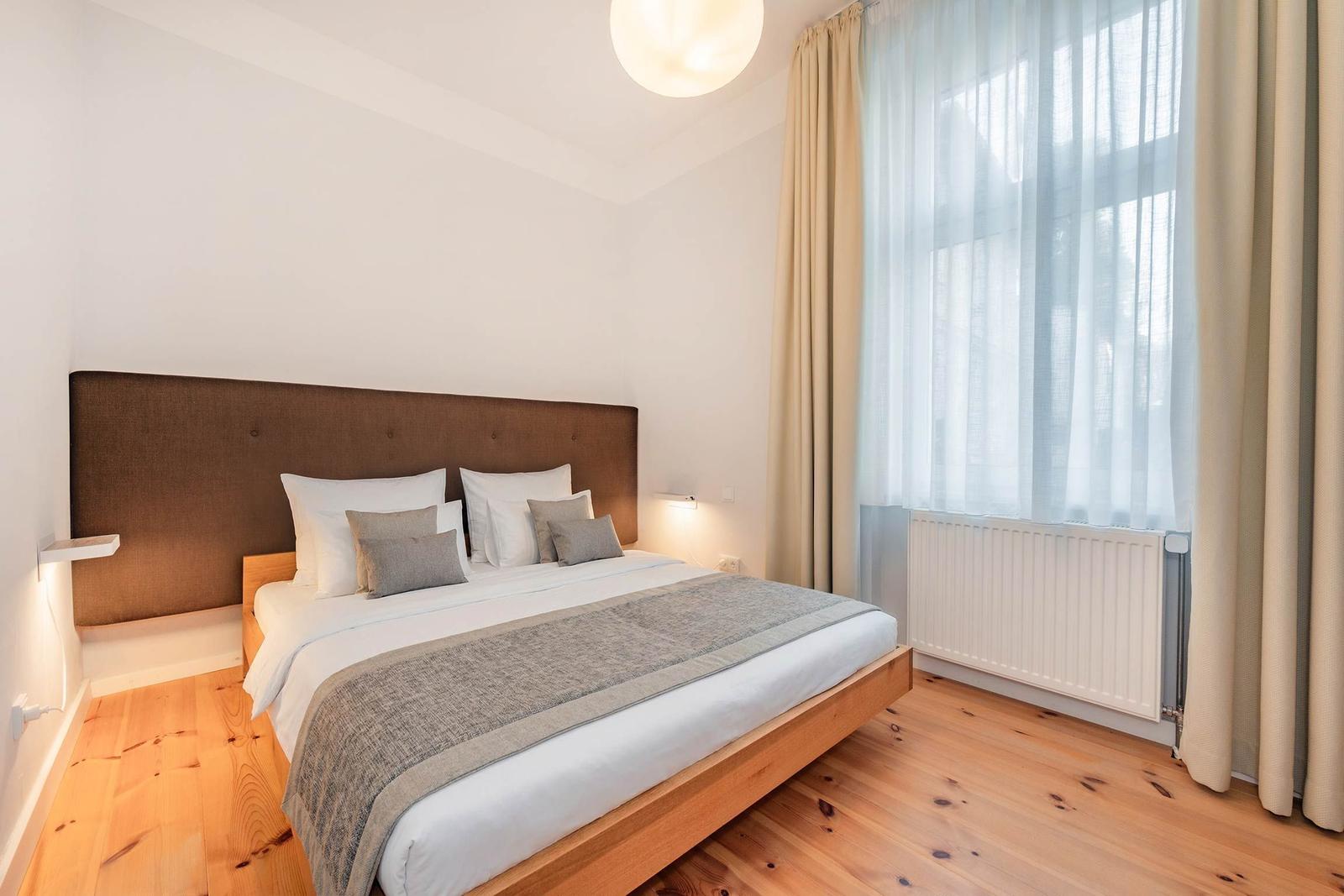 Ein Schlafzimmer mit einem Bett, Holzboden und großen Fenstern mit Vorhängen.