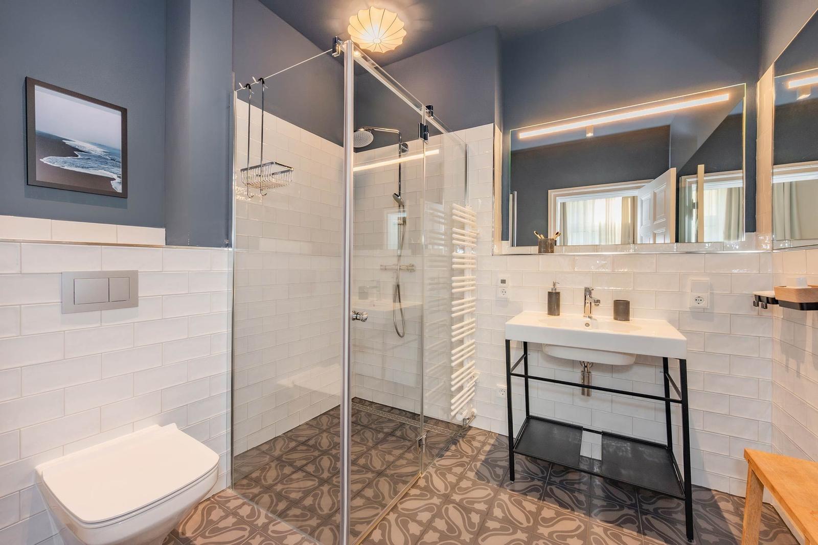 Badezimmer mit Dusche, Waschbecken und Toilette. Weiße Fliesen und dunkelblaue Wände.