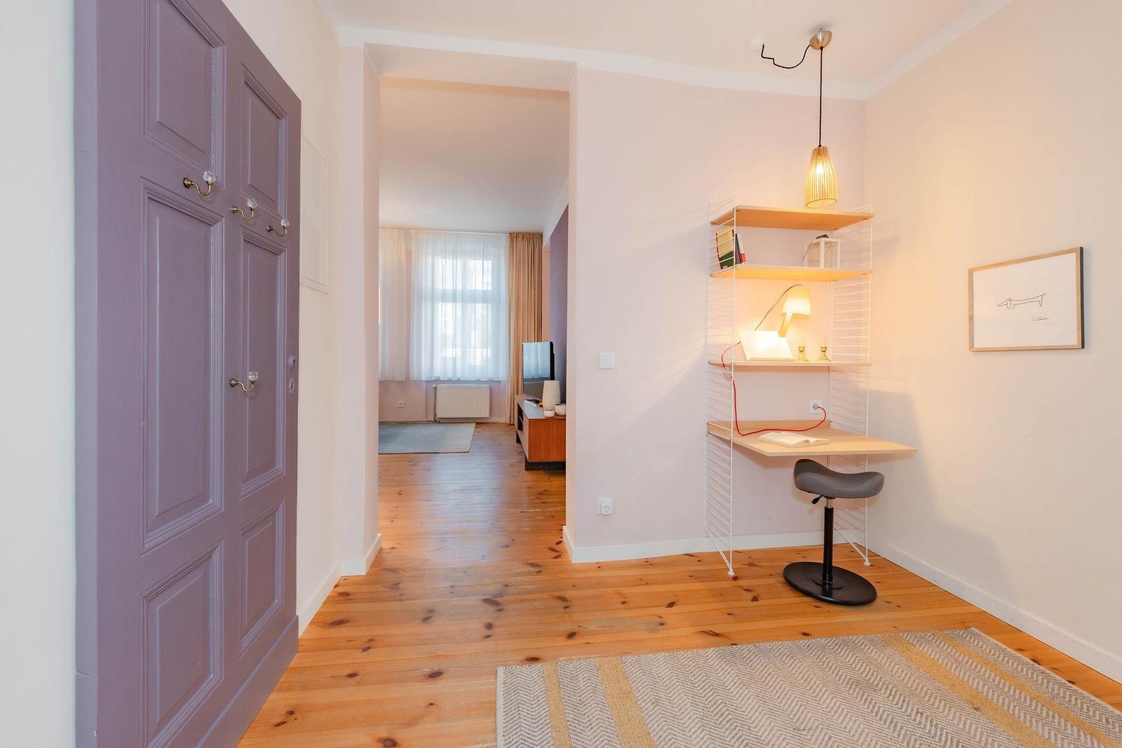 Helle Wohnung mit Holzboden, Schreibtisch und Kleiderschrank. Blick in Wohnzimmer mit Fenster.