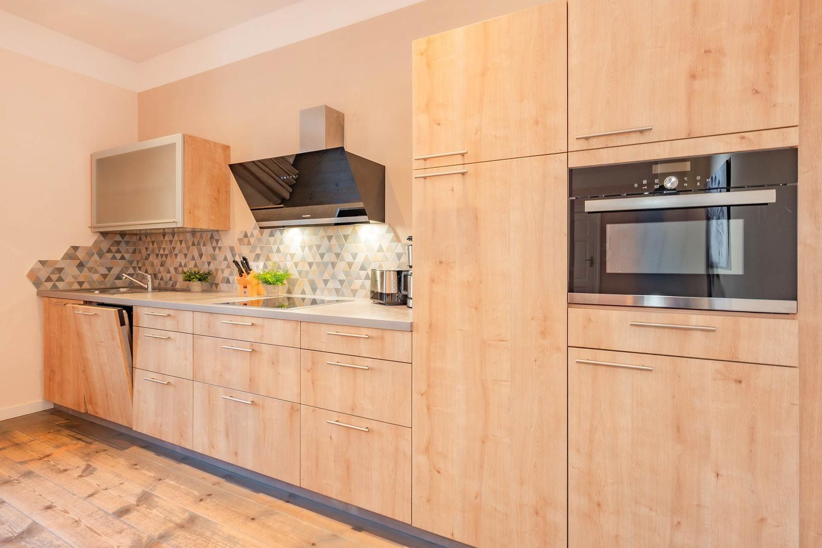 Moderne Küche mit Holzschränken, Edelstahlgeräten und geometrischem Fliesenspiegel.