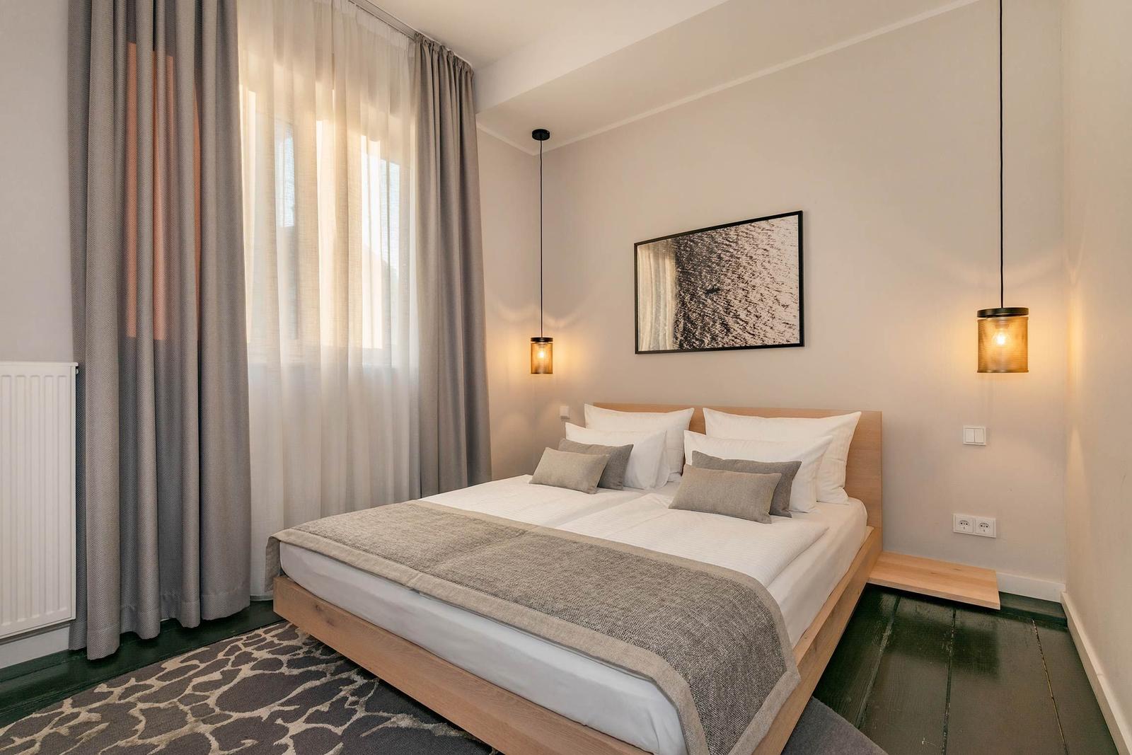 Schlafzimmer mit Doppelbett, Holzbettgestell, Vorhängen und Deckenleuchten.