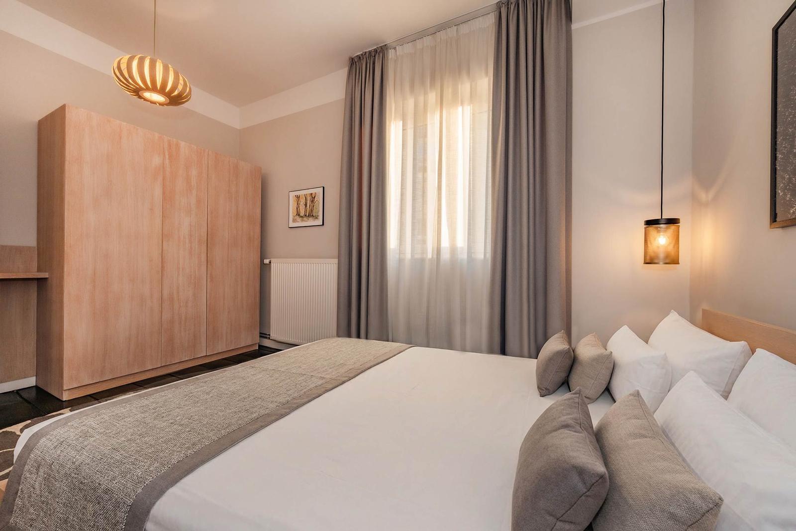 Schlafzimmer mit Bett, Kleiderschrank und Fenster mit Vorhängen.
