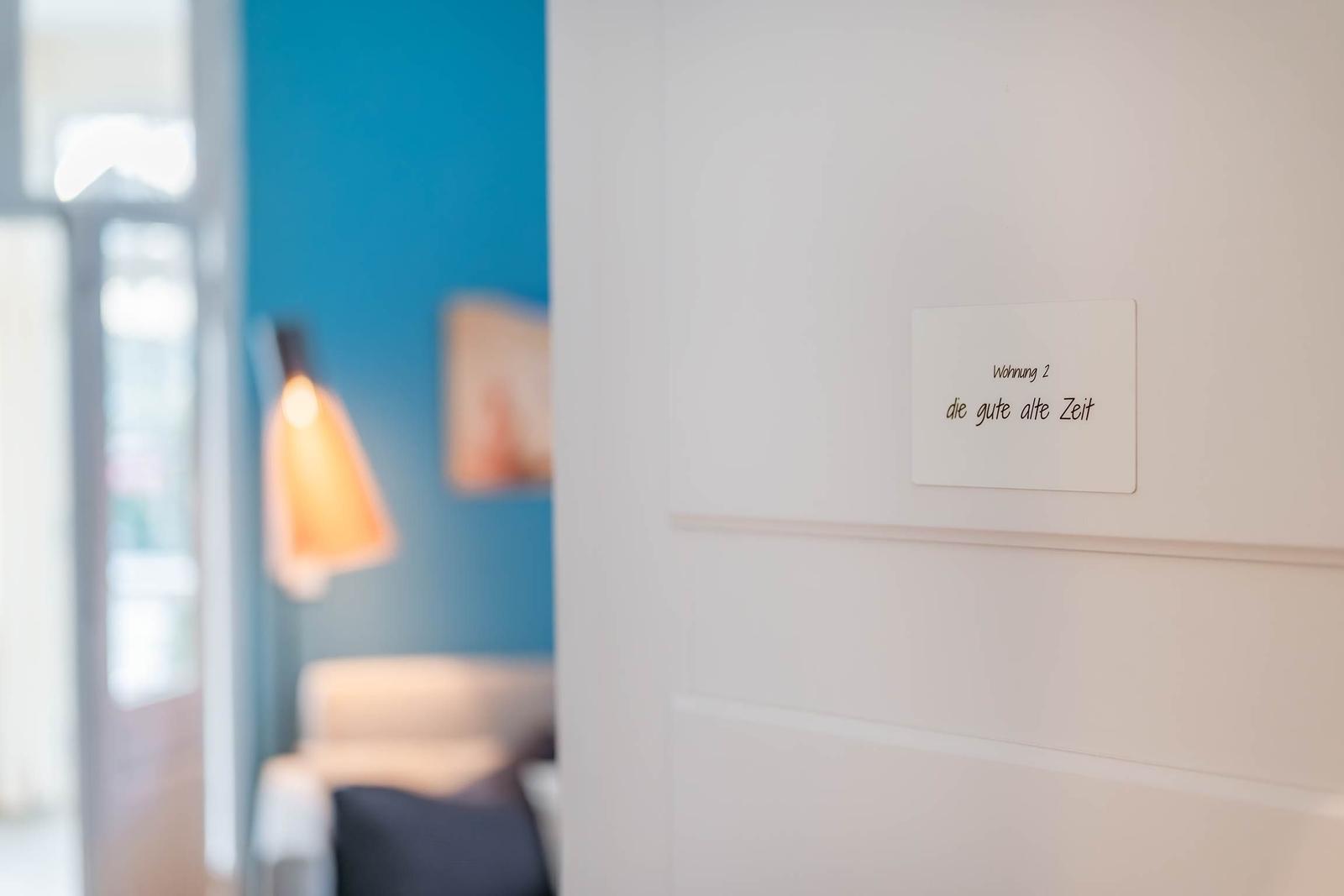 Türaufkleber zeigt Wohnung 2 mit Namen. Im Hintergrund ist ein Raum mit blauer Wand und Lampe.