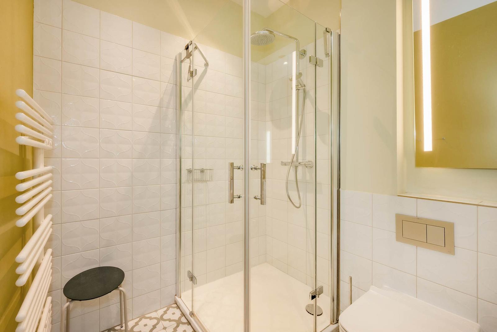 Dusche mit Glaswand, Toilette und Heizkörper an gelber Wand