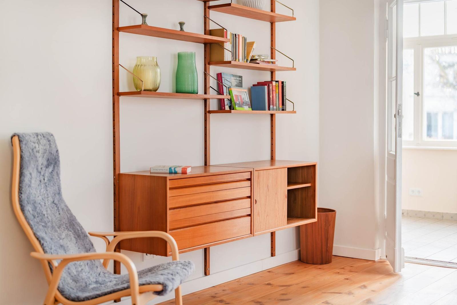 Holzregal mit Büchern und Vasen, Sessel und Tür zum Flur.