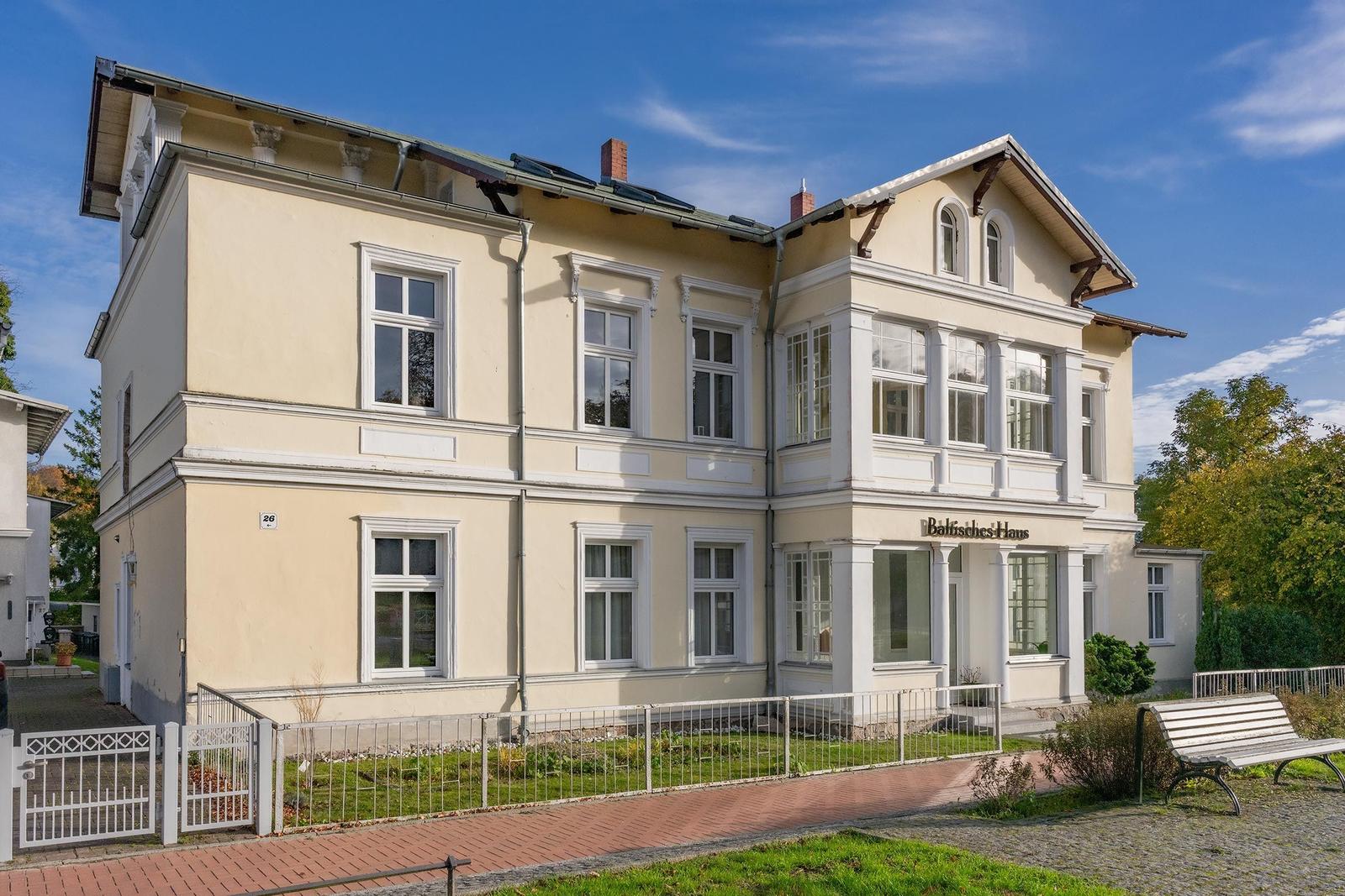 Ein zweistöckiges Haus mit weißen Fensterrahmen und einem Schild mit Baltisches Haus.