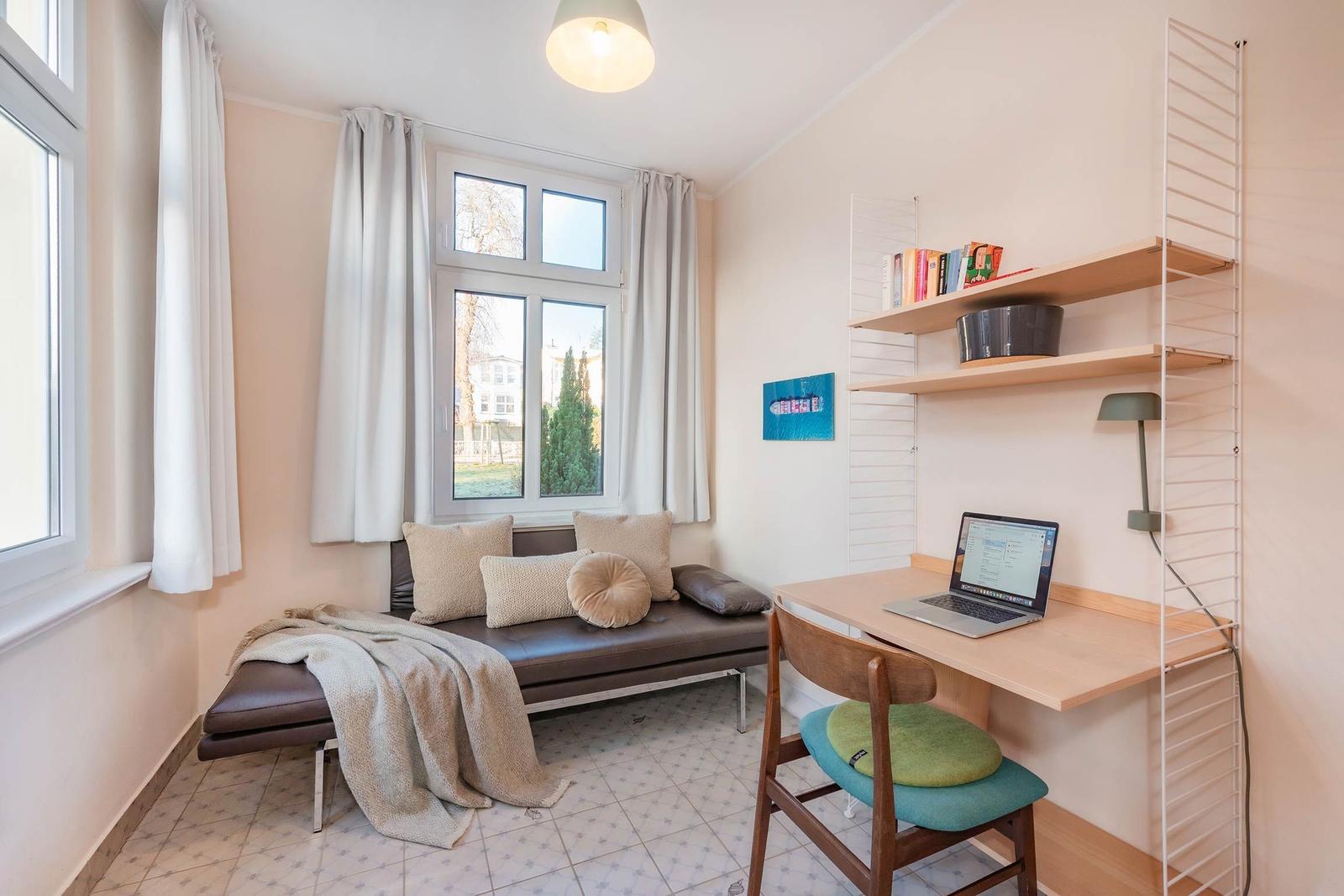 Ein Raum mit Fenster, Sofa, Schreibtisch und Regal.