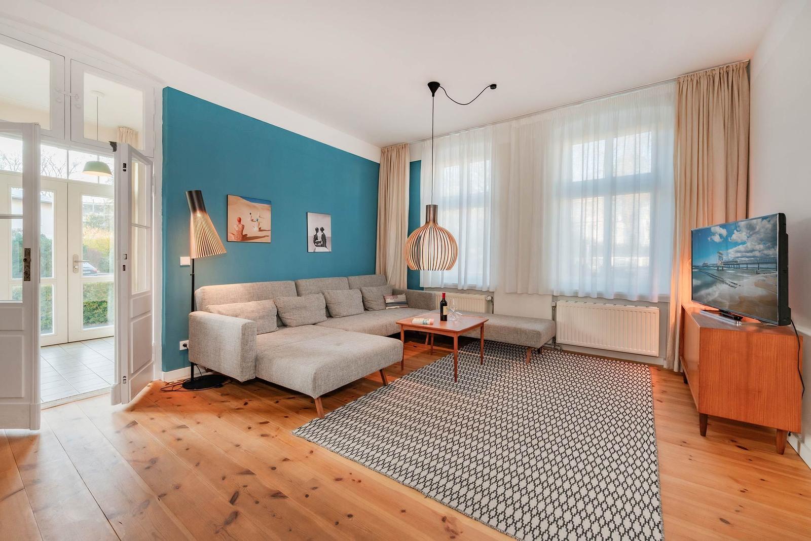 Wohnzimmer mit Sofa, Teppich und TV. Blaue Wand, Holzboden und Fenster mit Vorhängen.