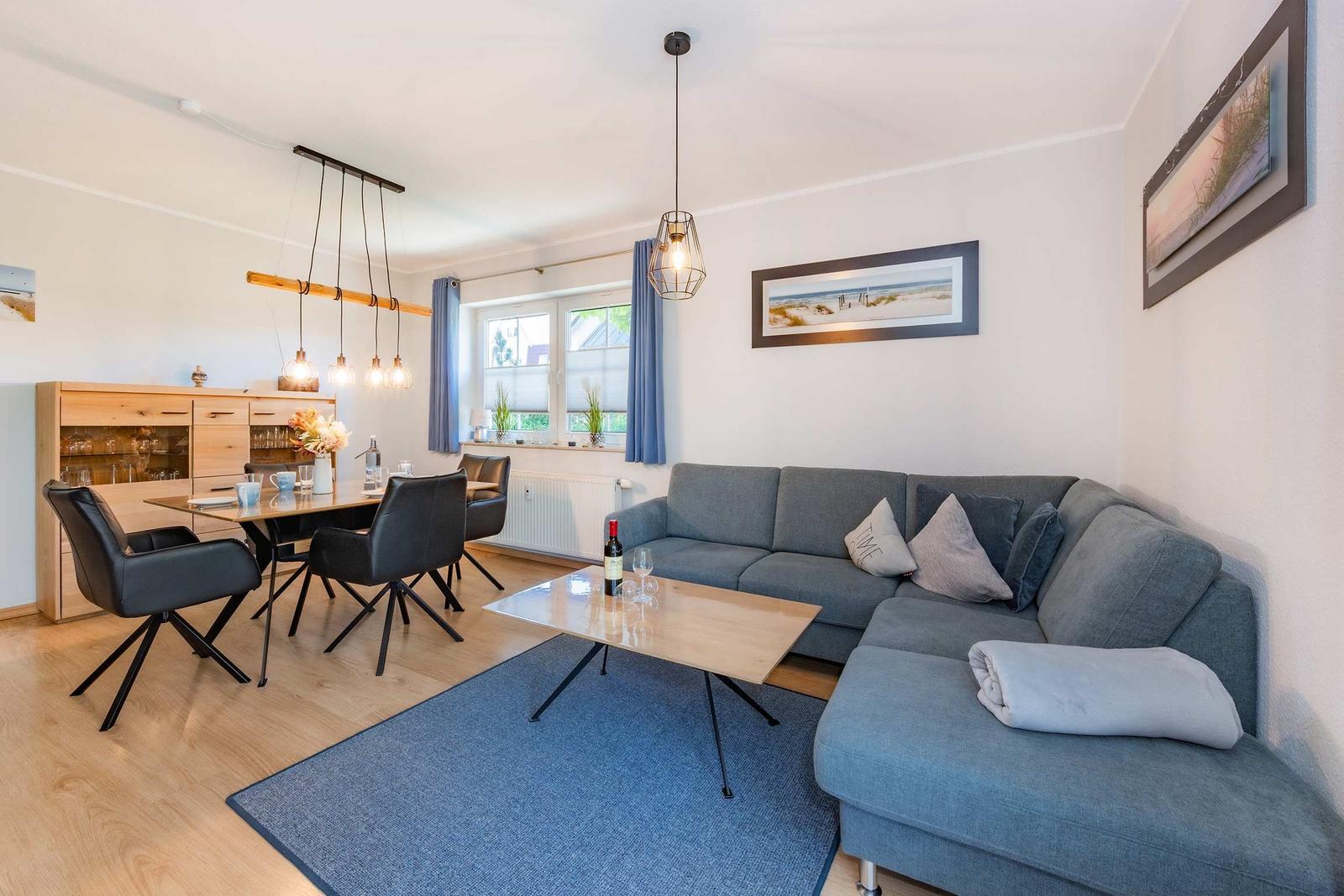 Wohn- und Essbereich mit Sofa, Tisch und Stühlen sowie Fenster mit Vorhängen.