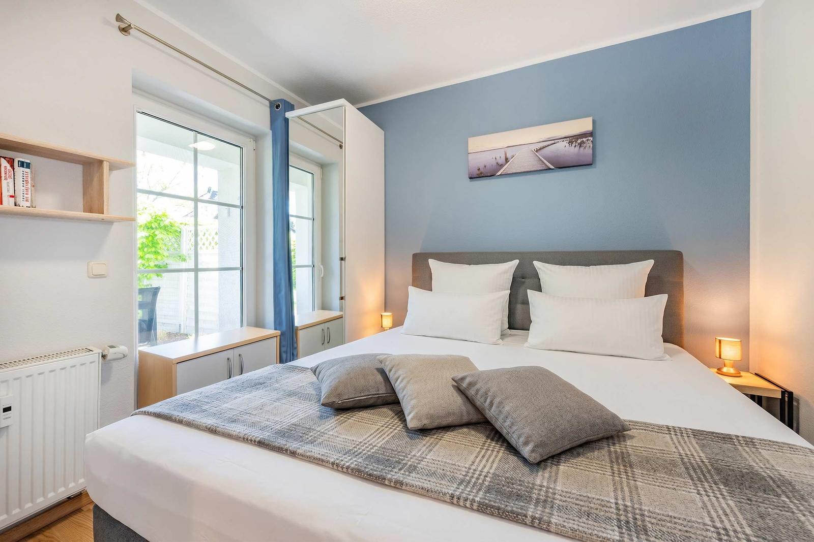 Schlafzimmer mit Bett, Wandbild und Fenster zur Terrasse.