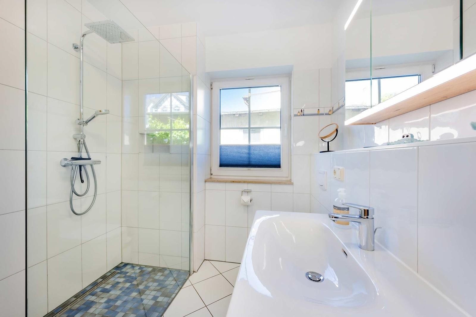 Badezimmer mit Dusche, Badewanne und Fenster. Weiße Fliesen und moderne Ausstattung.