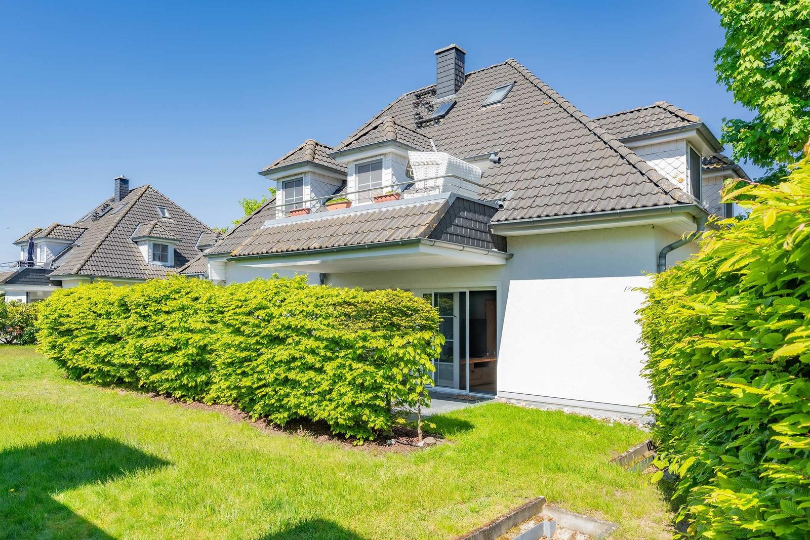 Ein Haus mit Dachgauben und Balkon, umgeben von grünem Rasen und Hecken.
