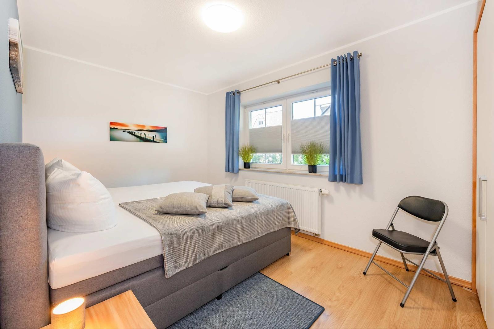 Schlafzimmer mit Bett, Stuhl und Fenster mit Vorhängen.