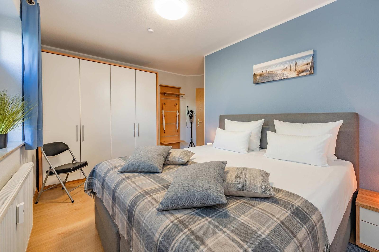 Schlafzimmer mit Bett, Kleiderschrank und Wandbild.