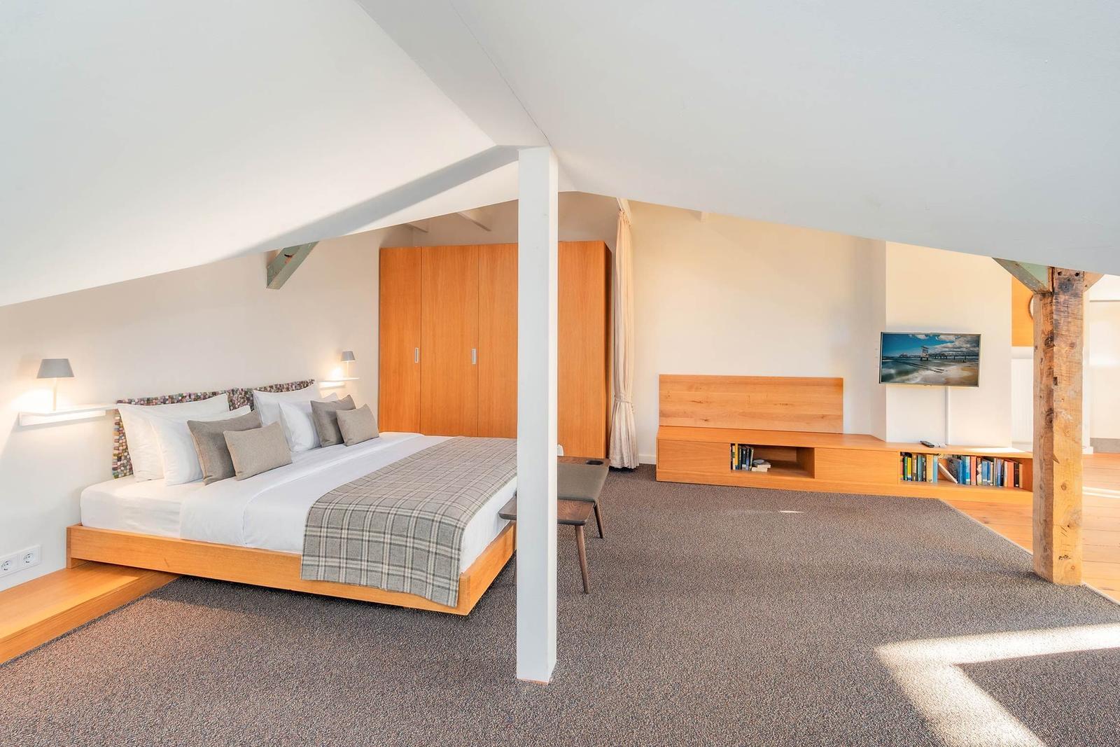 Schlafzimmer mit Bett, Kleiderschrank und TV-Bereich unter Dachschrägen.