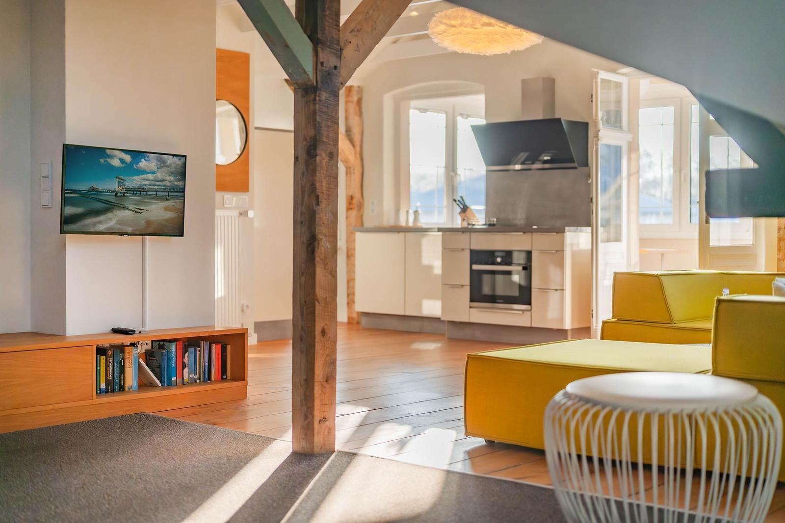 Wohnzimmer mit gelbem Sofa, Küchenbereich und Fernseher an der Wand.