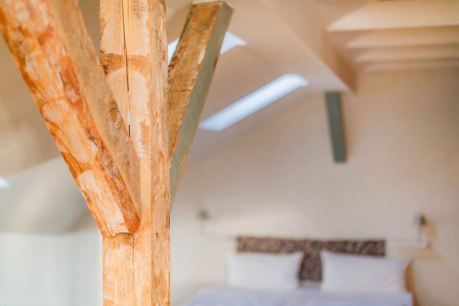 Schlafzimmer mit Holzbalken und Dachschräge. Bett mit Kissen im Hintergrund.