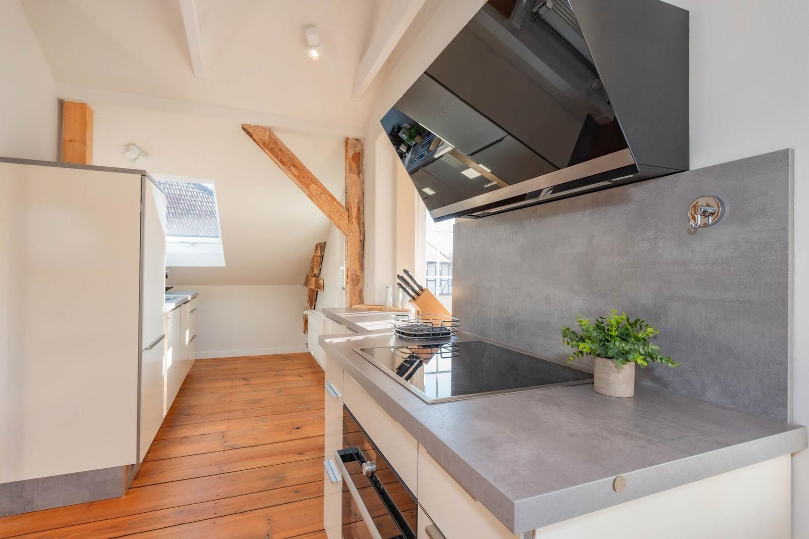 Küche mit moderner Kochplatte, Dunstabzug und Holzbalken an der Decke.