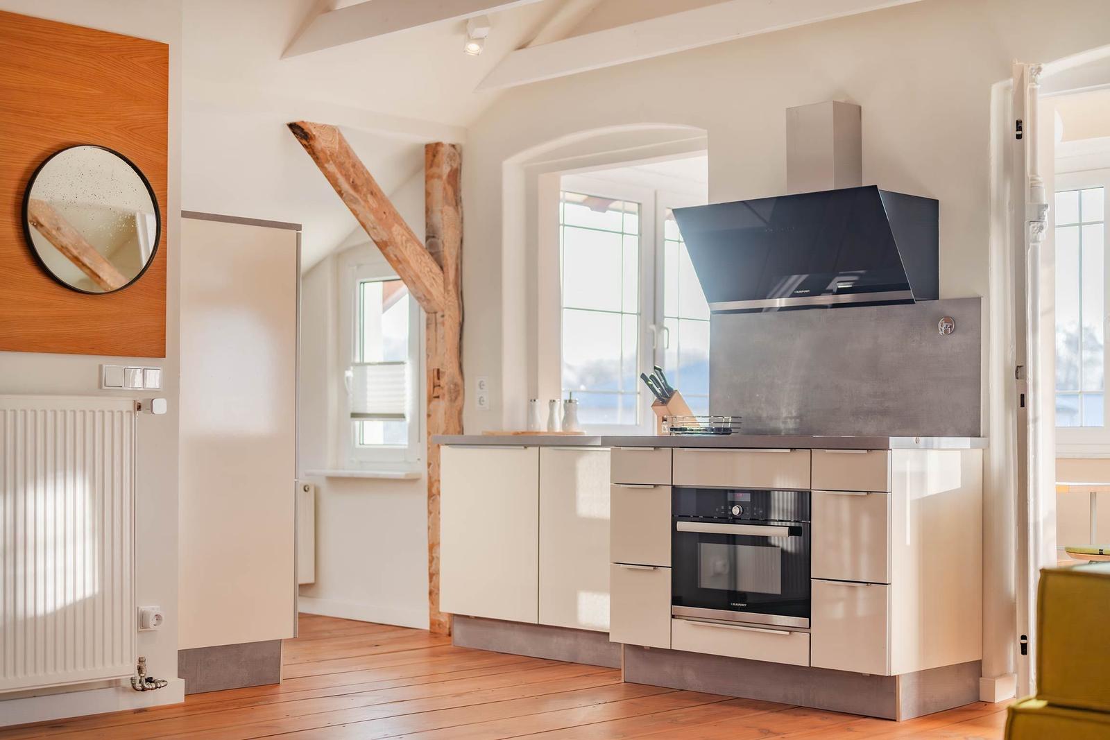 Küche mit moderner Einbauküche, Holzbalken und Fenster. Holzfußboden und runder Spiegel.