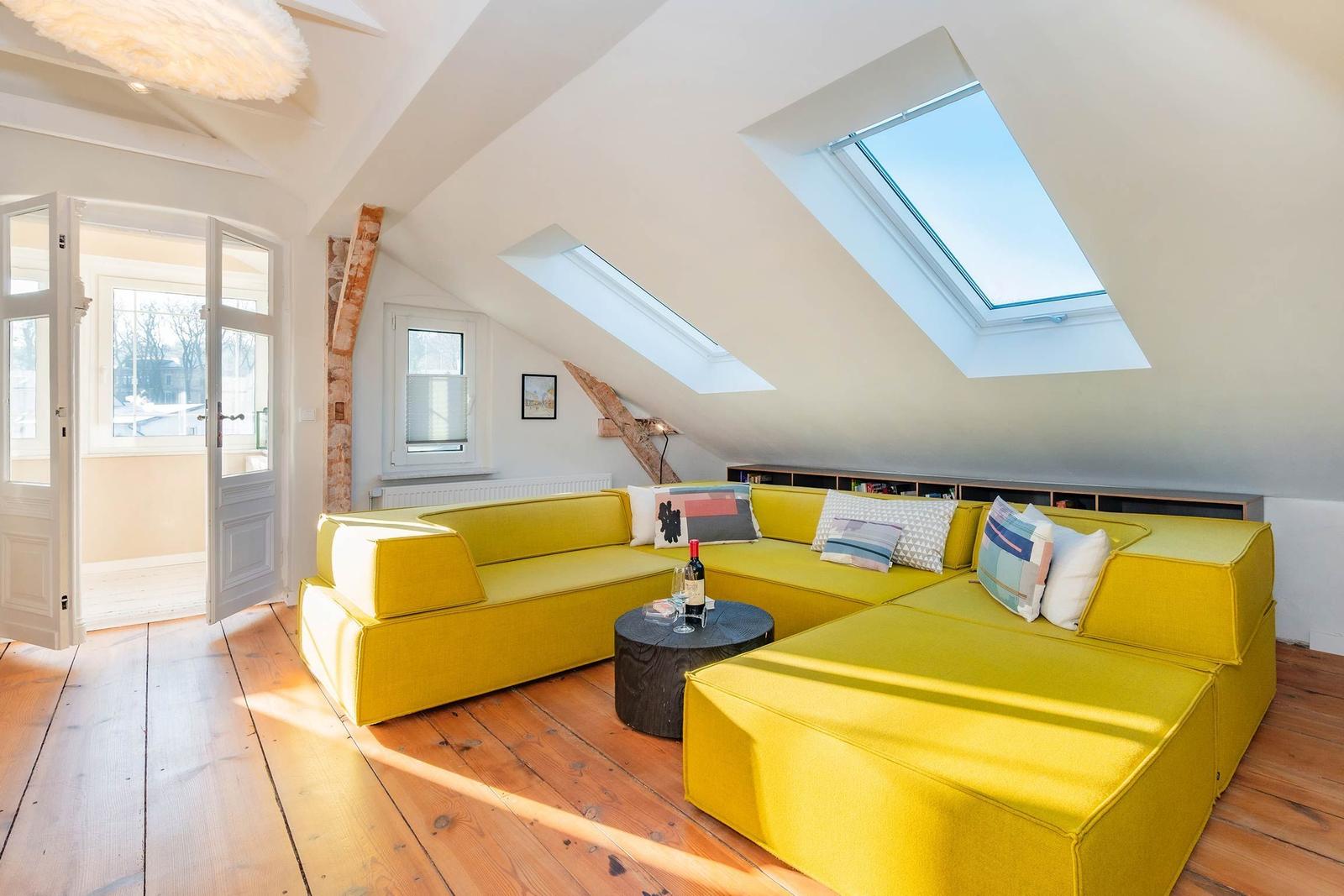 Dachgeschosswohnung mit gelbem Sofa, Holzboden und Dachfenstern.