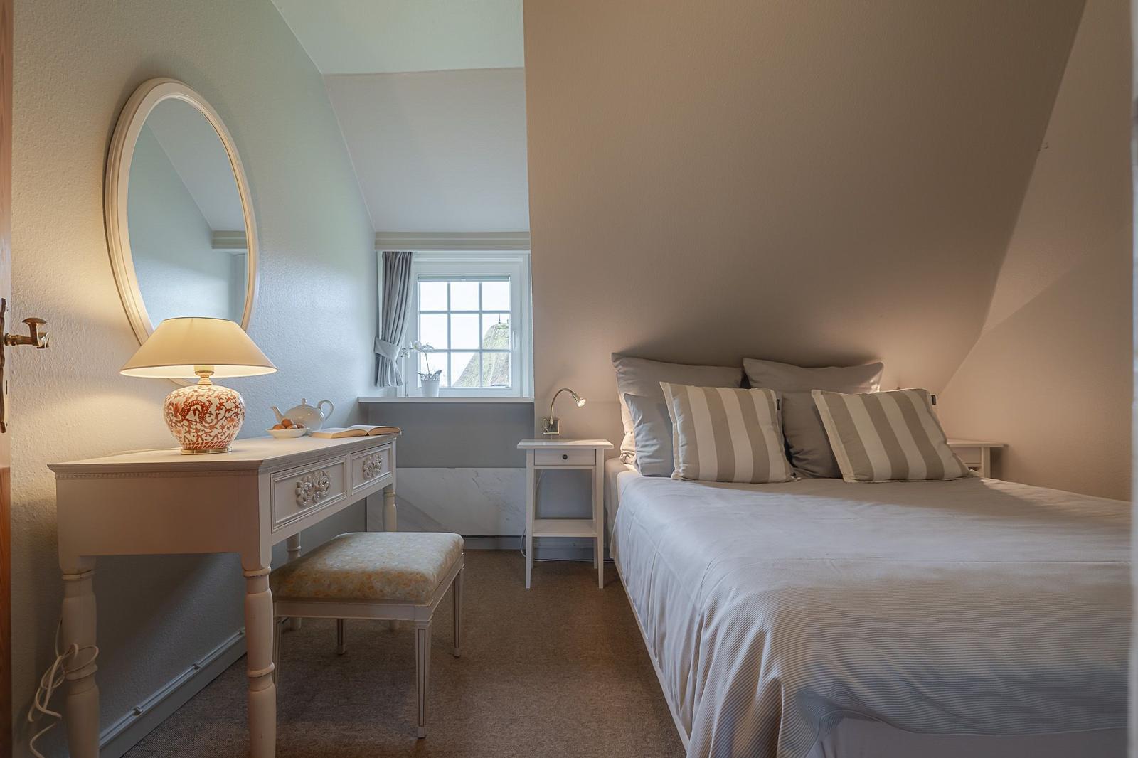 Schlafzimmer mit Doppelbett, Schreibtisch und Fenster. Decke ist schräg.