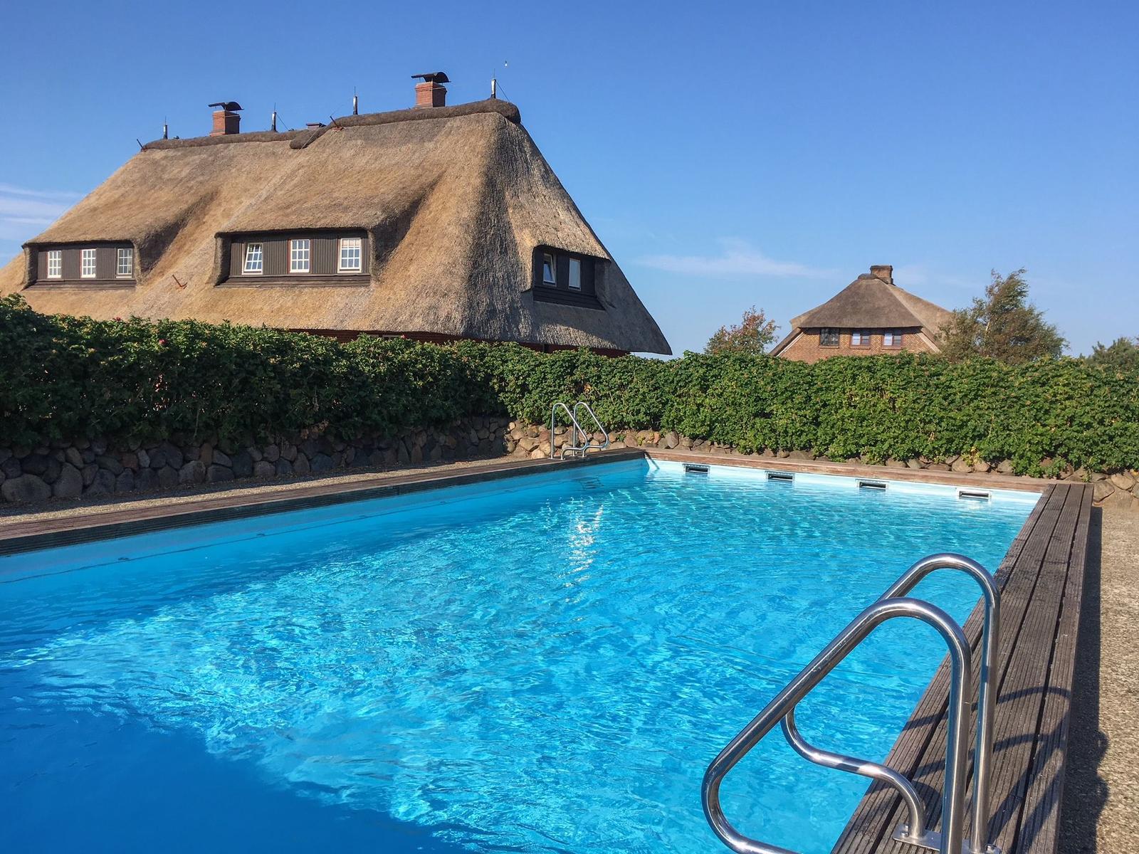 Pool mit Holzdeckung und Stufen. Im Hintergrund Thatched House mit grüner Hecke.