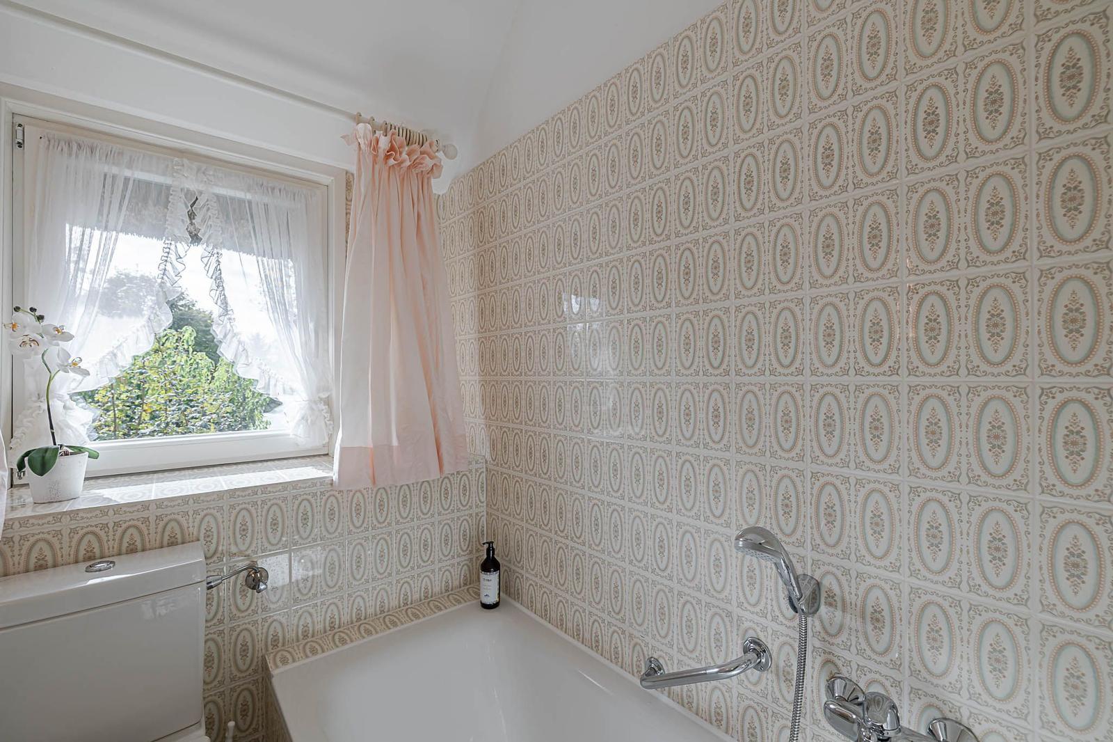 Badezimmer mit Badewanne, Fenster und floralen Fliesen