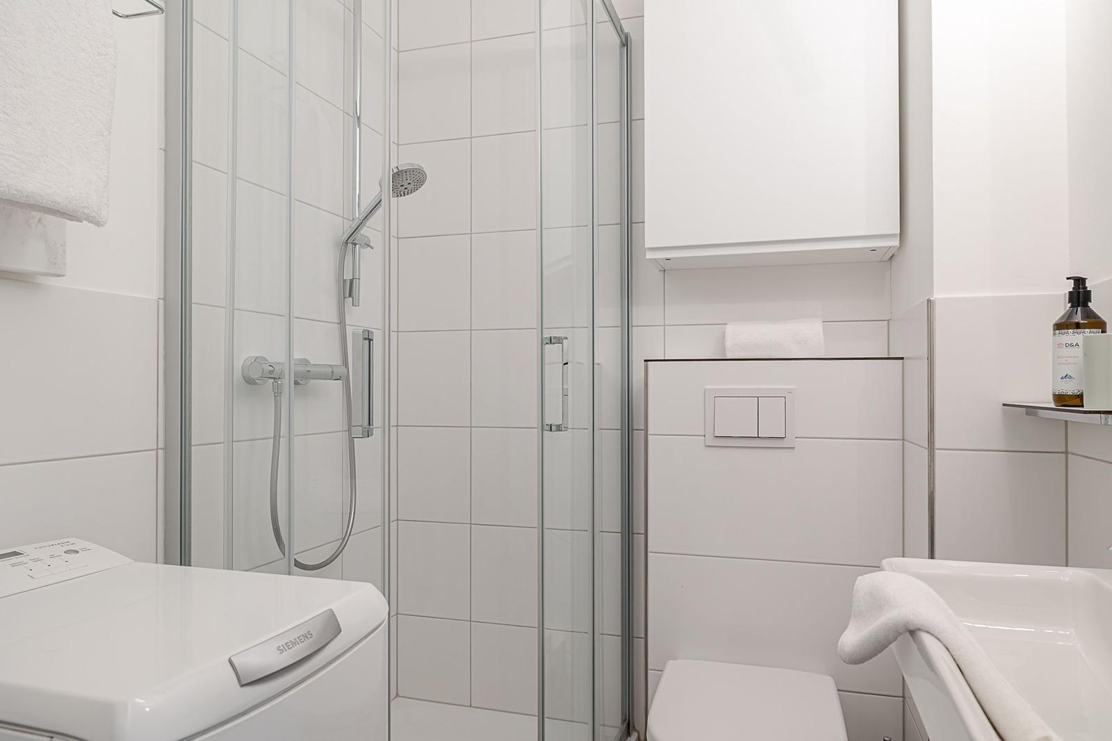 Badezimmer mit Dusche, Toilette und Waschmaschine.