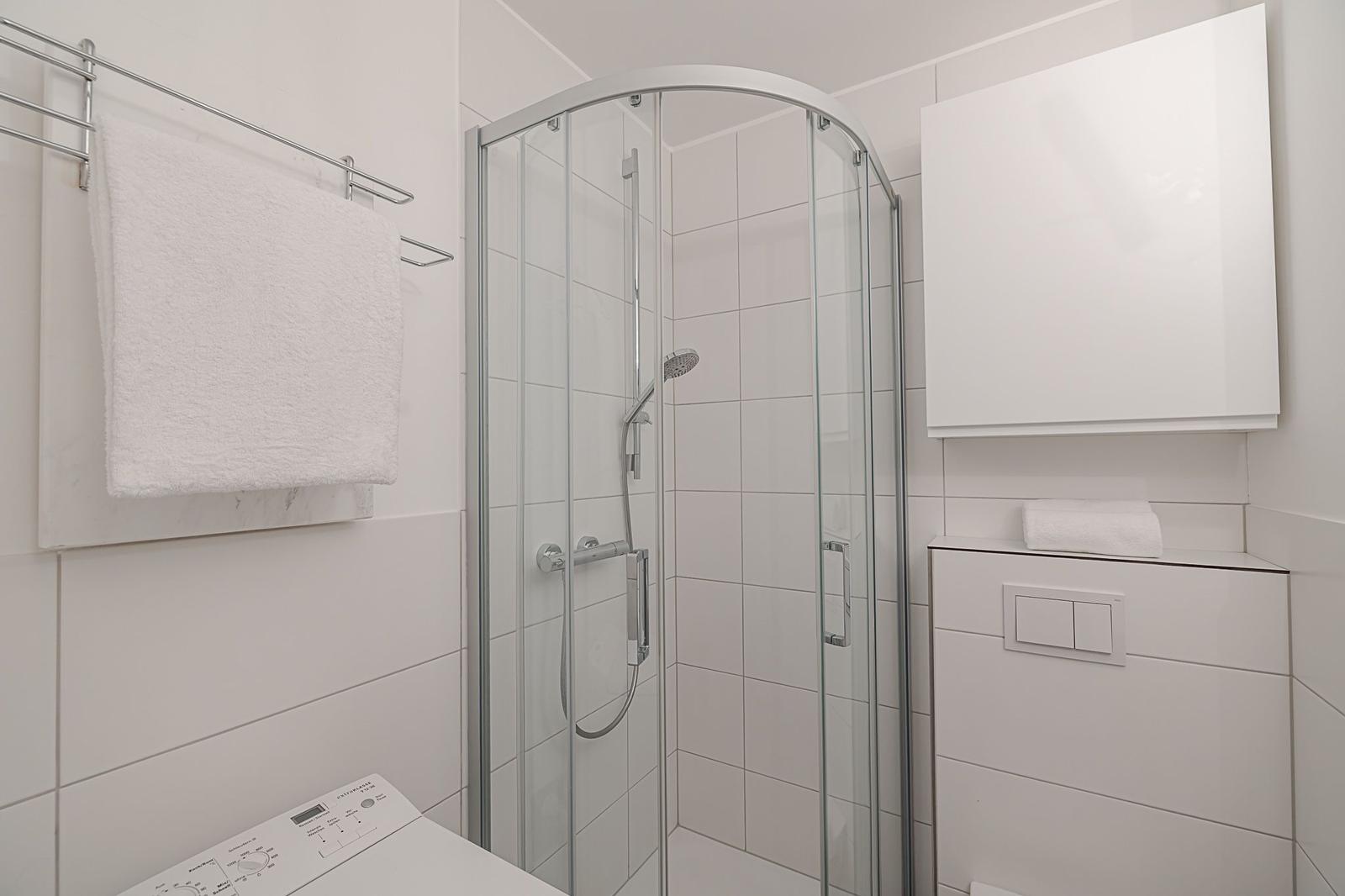 Badezimmer mit Dusche, Handtuchhalter und Waschmaschine.