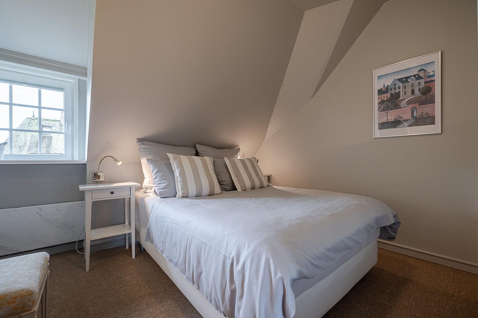 Schlafzimmer mit Bett, Nachttisch und Fenster. Decke geneigt. Wandbild an der Wand.