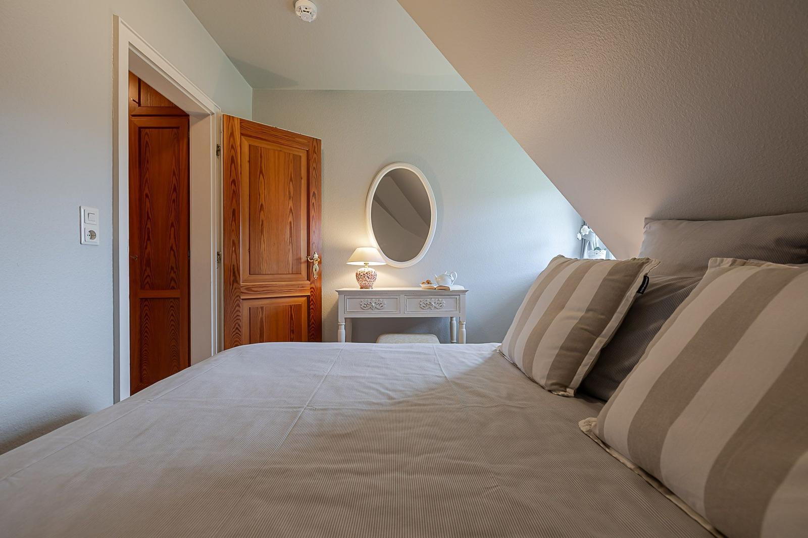 Schlafzimmer mit Bett, Schminktisch und Holztüren unter Dachschrägen.