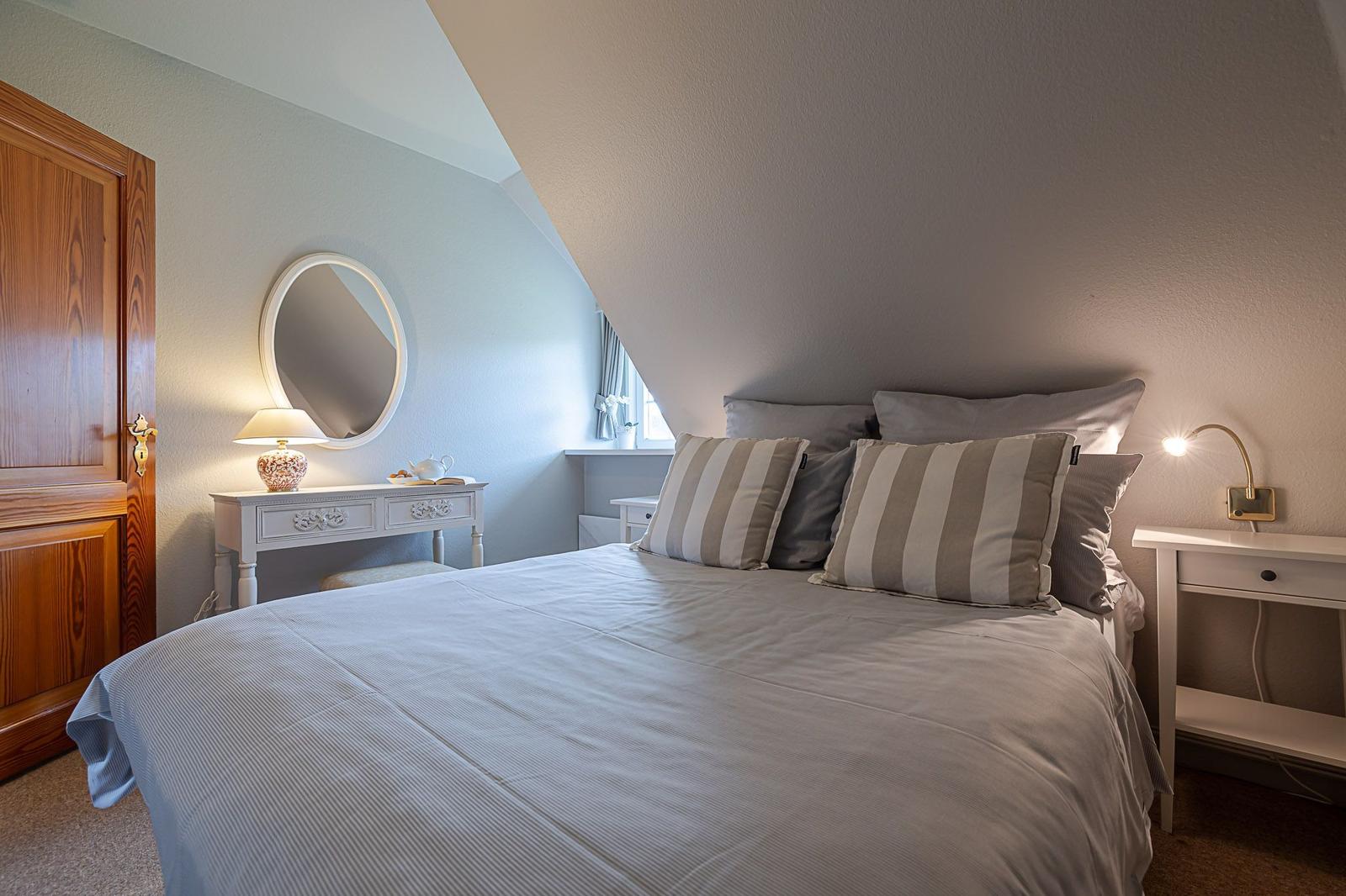 Schlafzimmer mit Dachschrägen, Bett, Nachttisch und Schminktisch mit Spiegel.