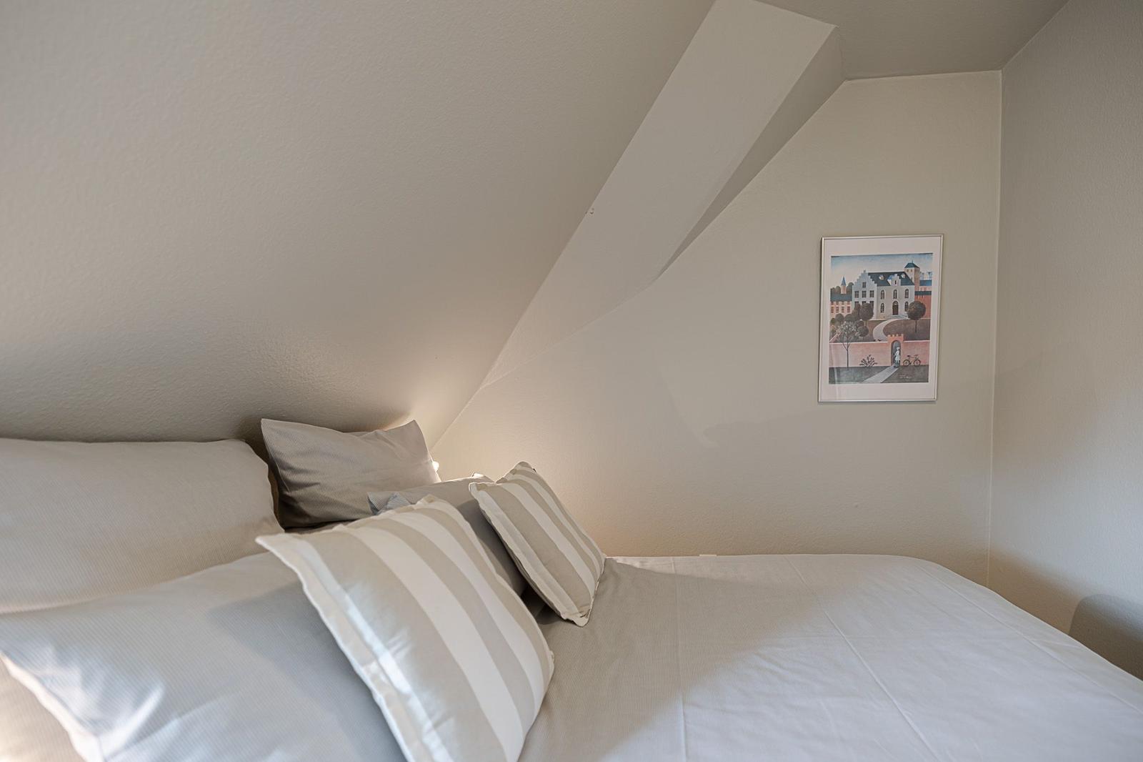 Schlafzimmer mit Bett, Kissen und Wandbild unter schrägem Dach