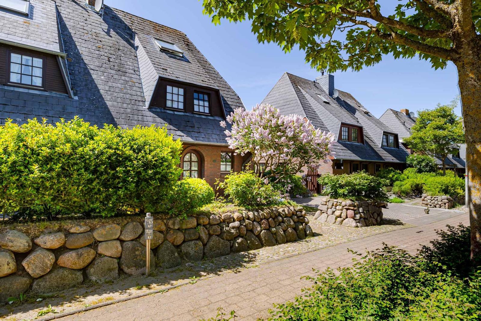 Haus mit Steinmauer, Blumen und Schieferdach unter blauem Himmel.
