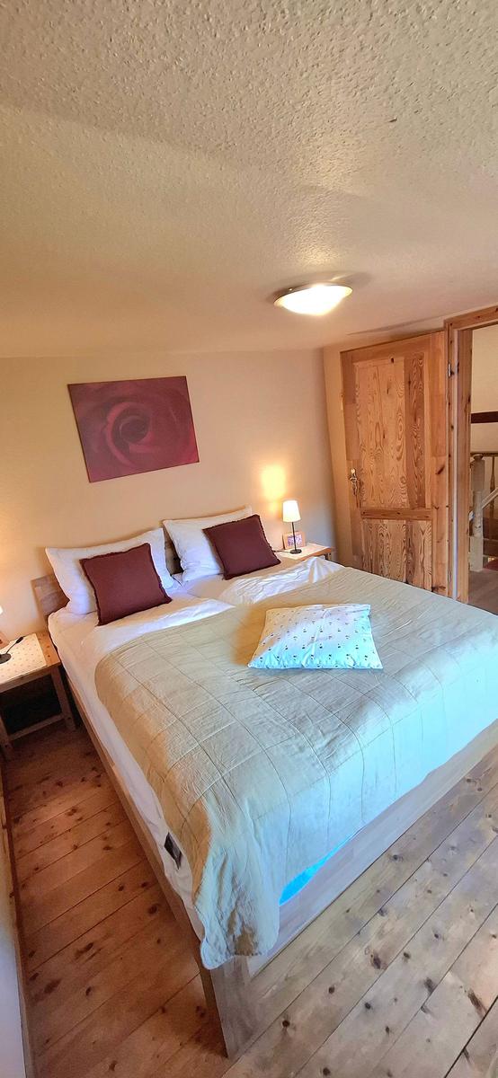 Ein Schlafzimmer mit Doppelbett, Holzboden und Wandbild. Neben dem Bett steht eine Nachttischlampe.