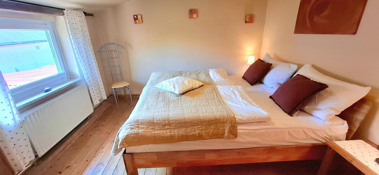 Ein Schlafzimmer mit Doppelbett, Fenster, Heizkörper und Holzboden.