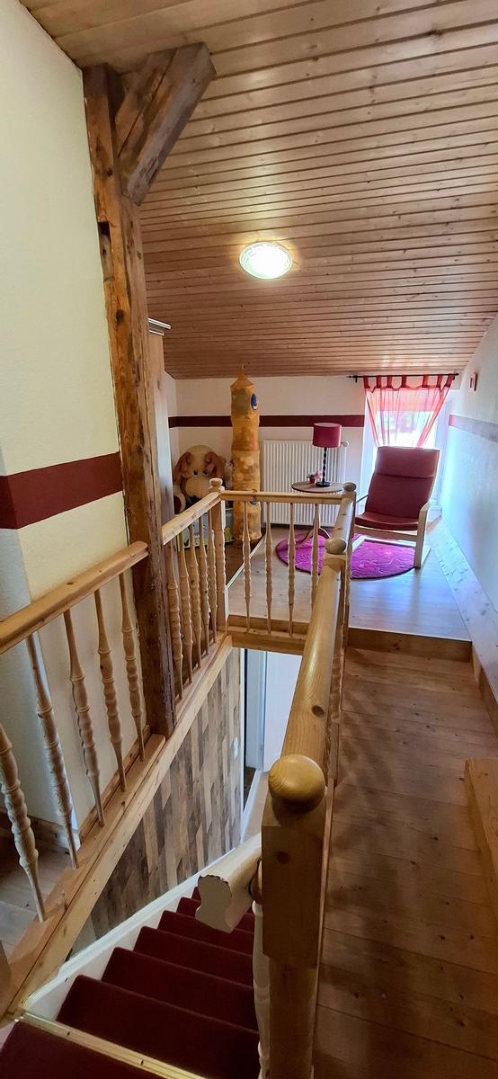 Holzgetäfelte Decke, Holzstufen mit rotem Teppich und Sitzgelegenheit im Obergeschoss.