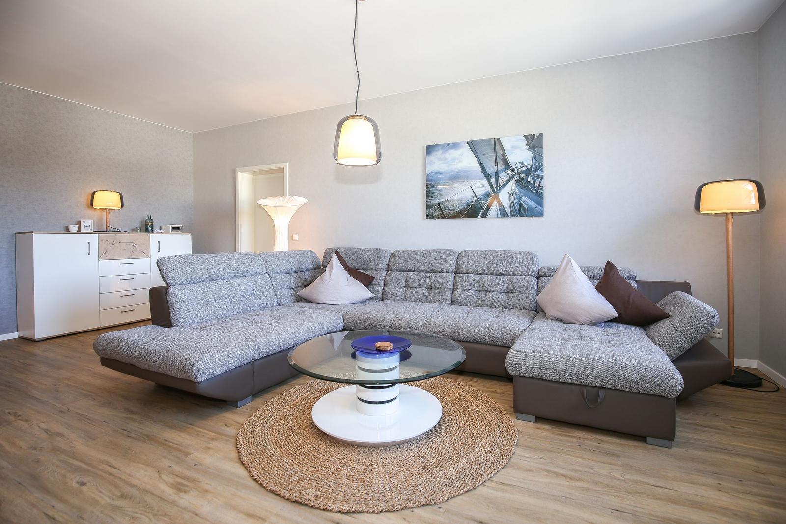 Wohnzimmer mit grauem Sofa, Glas-Tisch und Wandbild mit Segelyacht.