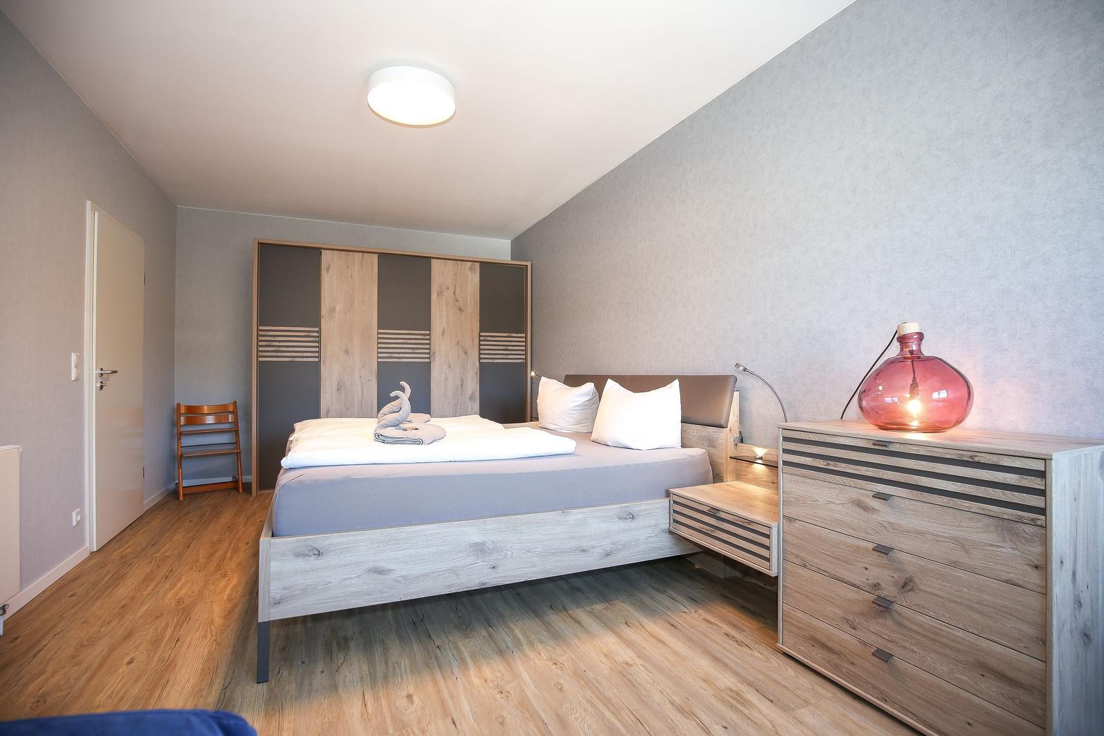 Schlafzimmer mit Bett, Kleiderschrank und Schminktisch mit Lampe.