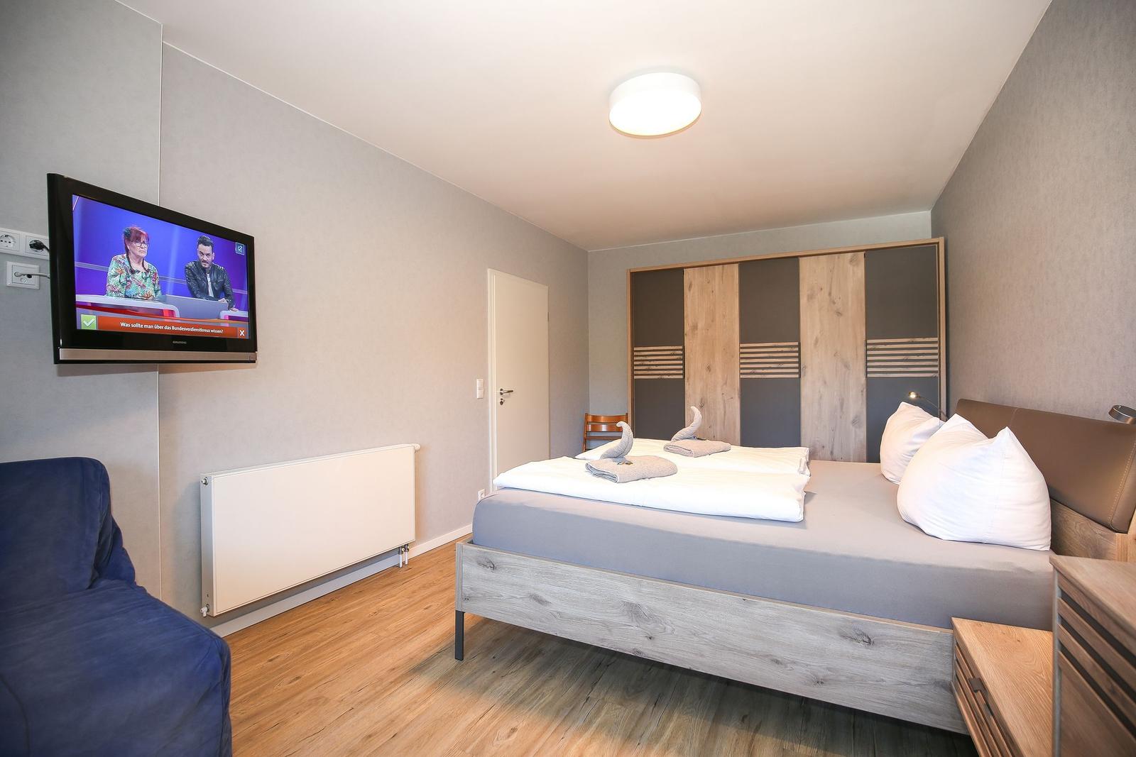 Schlafzimmer mit Bett, Kleiderschrank und Wandfernseher.