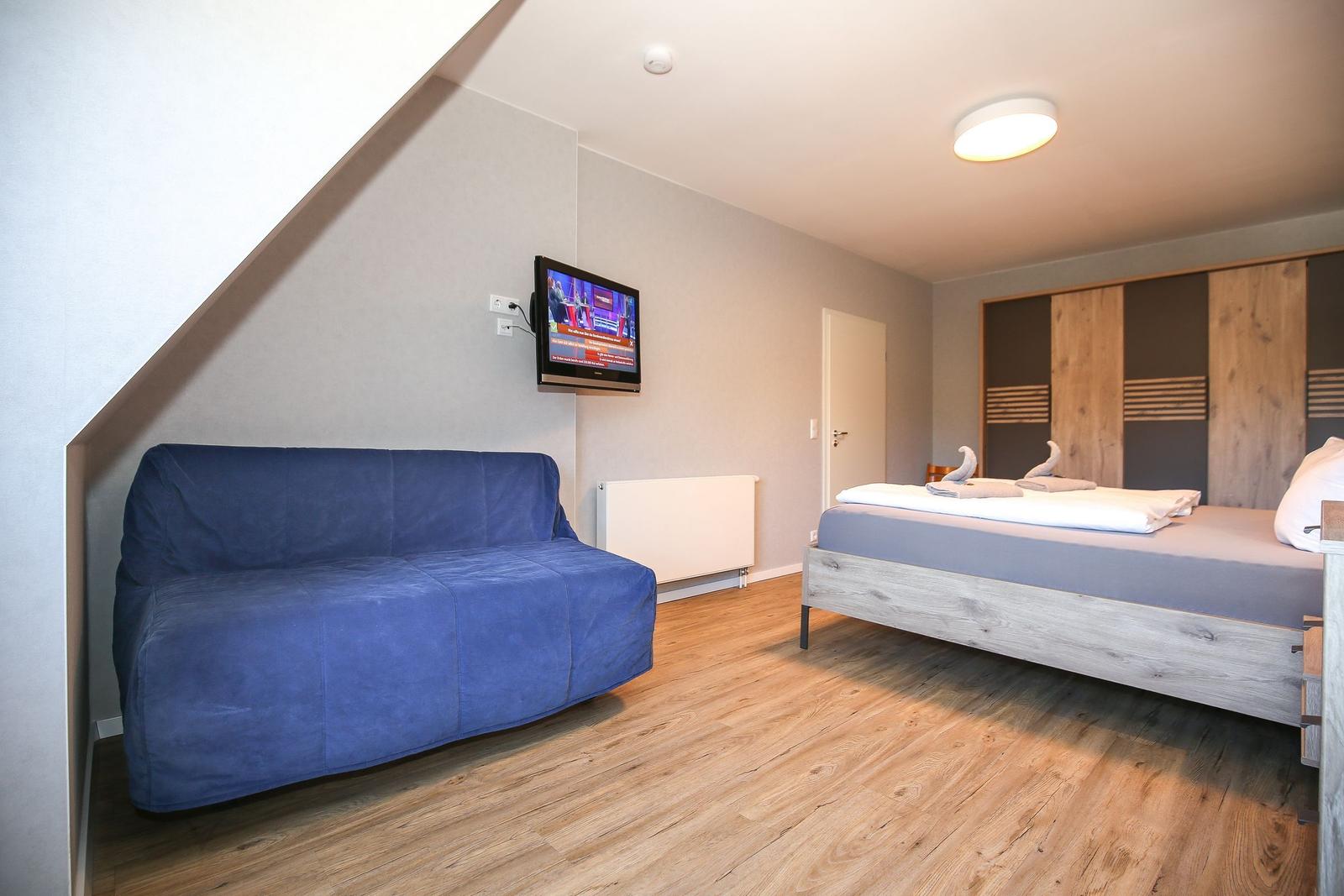 Schlafzimmer mit Bett, Sofa und Fernseher an der Wand.