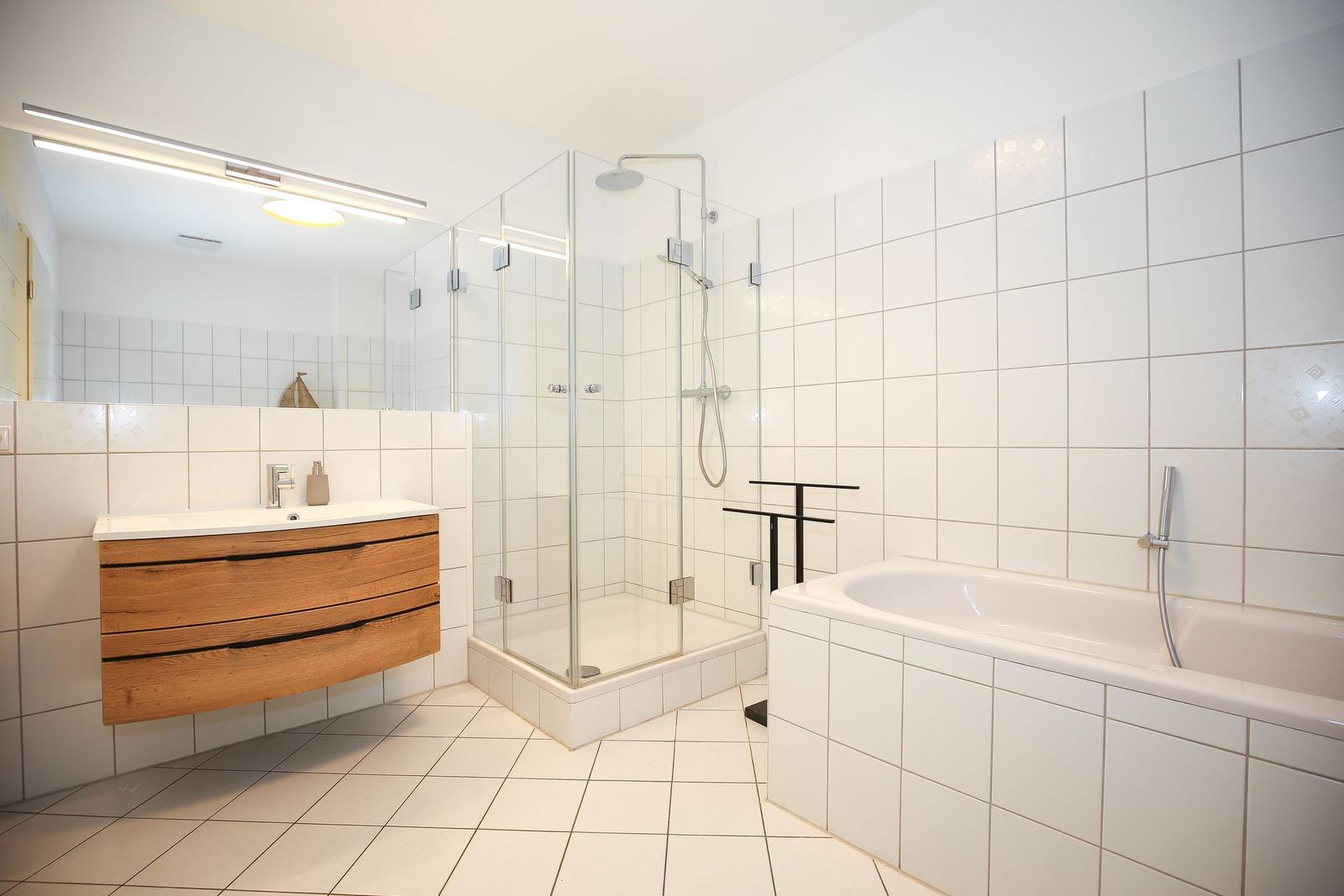 Badezimmer mit Dusche, Badewanne und Holzwaschtisch.