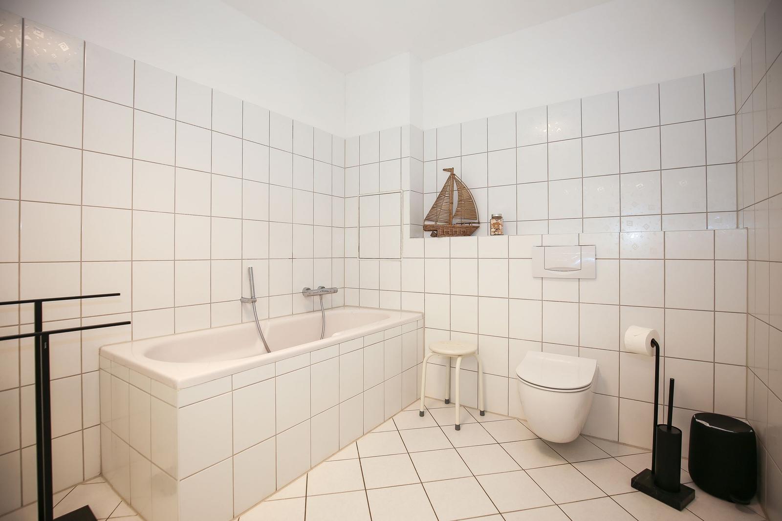 Bad mit Badewanne, WC und kleinem Hocker. Wanddekoration mit Segelboot.