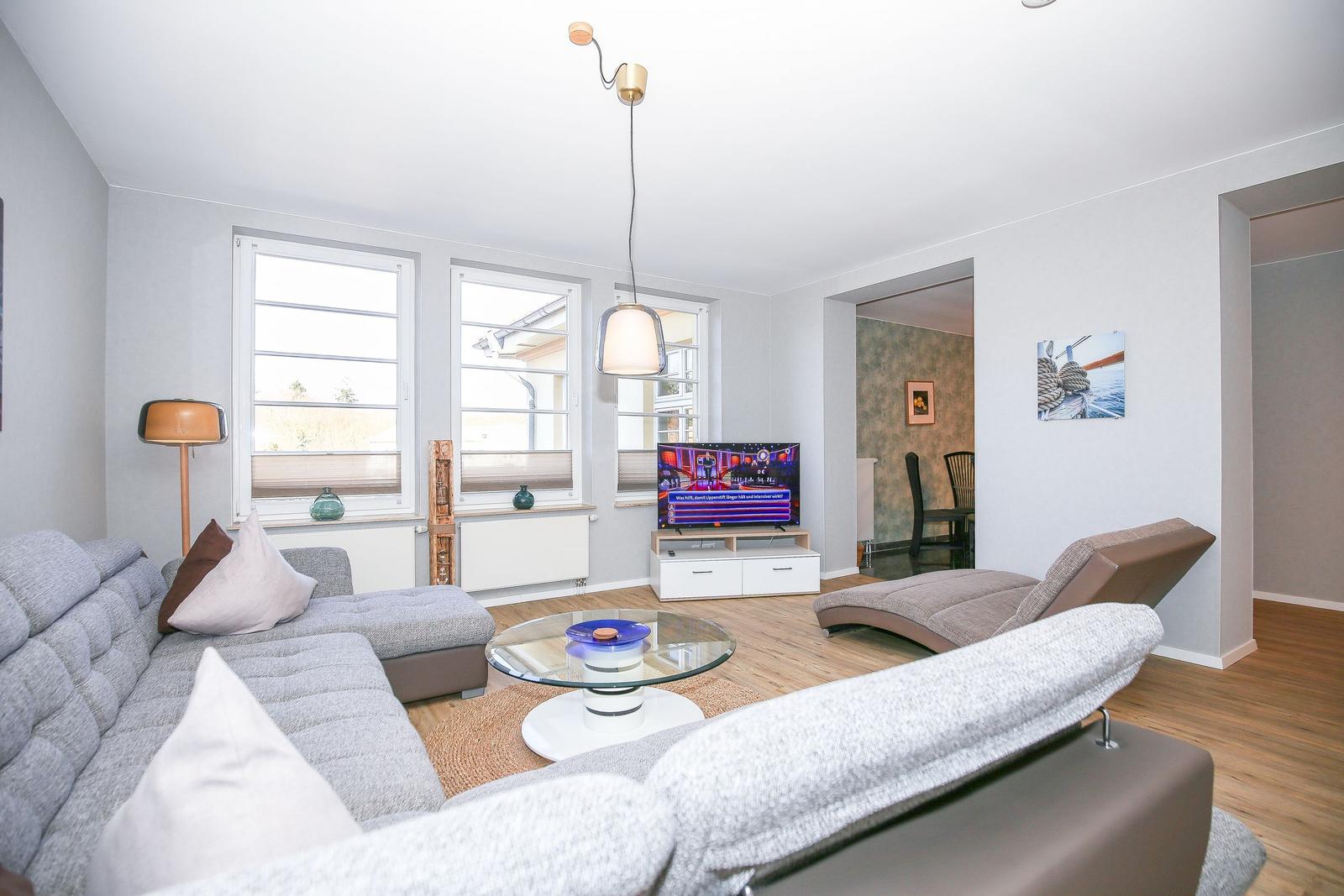 Wohnzimmer mit Sofa, Couchtisch und Fernseher. Durchgänge zu anderen Räumen.