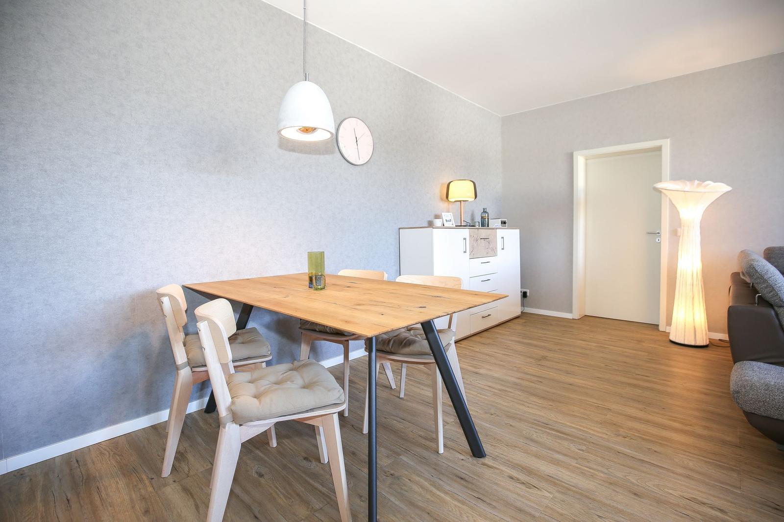 Essbereich mit Holztisch, Stühlen und Wanduhr. Helle Beleuchtung und Holzfußboden.