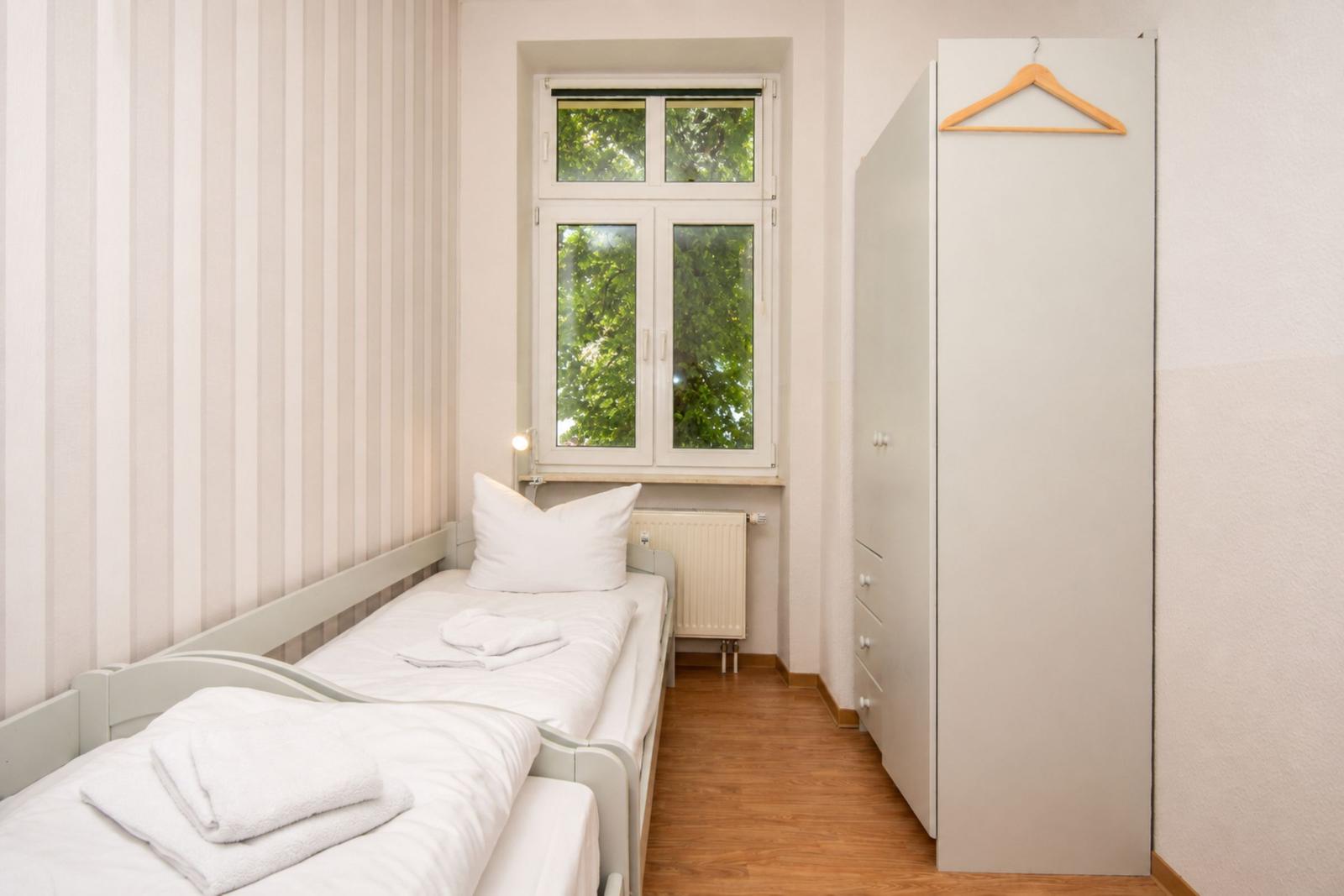 Ein Schlafzimmer mit einem Bett, einem Kleiderschrank und einem Fenster mit Blick auf Bäume.