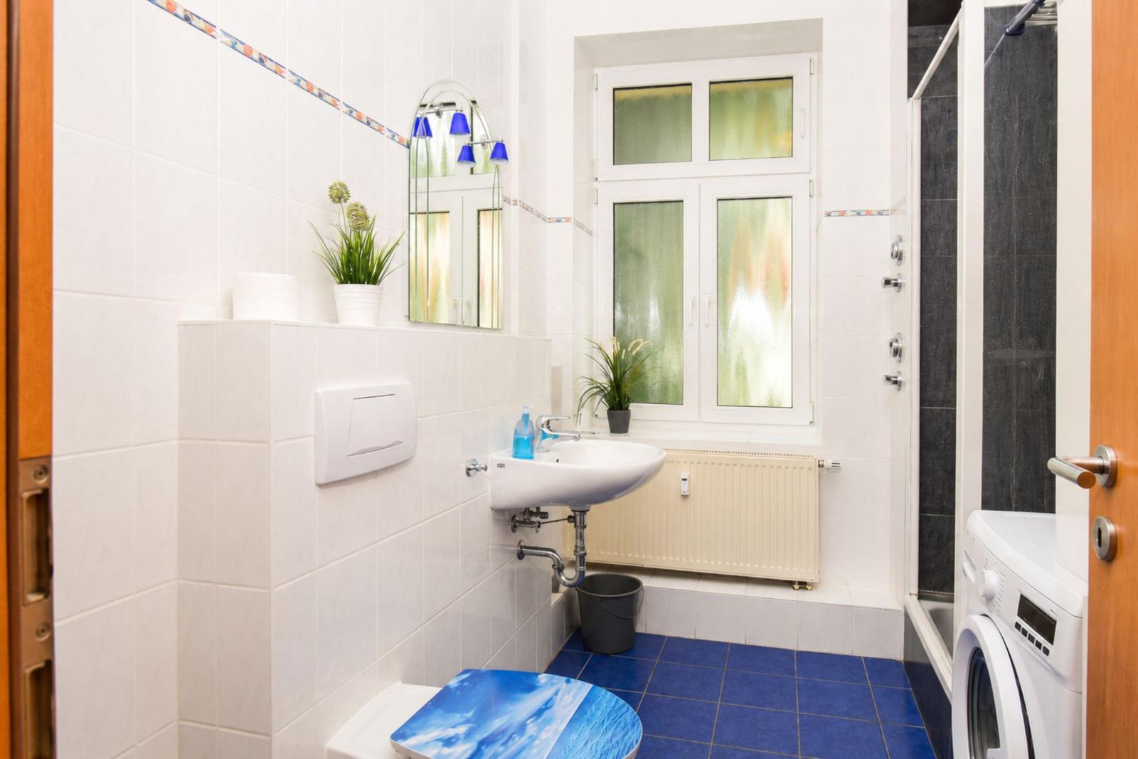 Badezimmer mit Waschmaschine, Dusche und Fenster mit getöntem Glas.