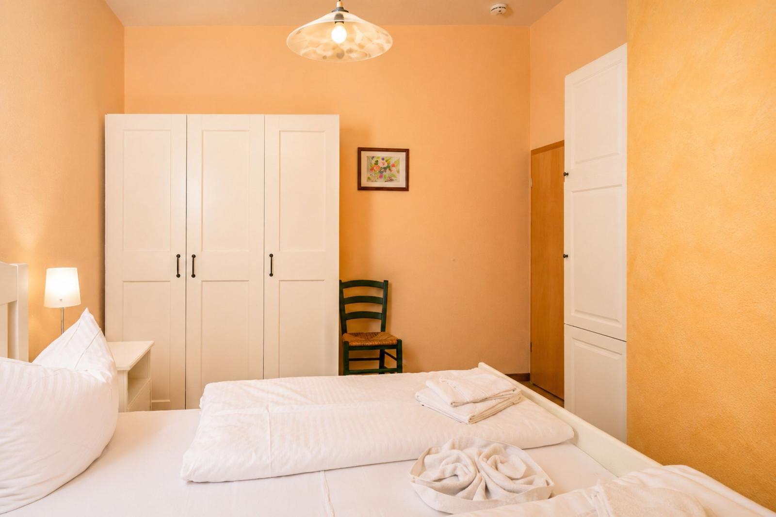 Schlafzimmer mit weißem Bett, Kleiderschrank und grüner Stuhl.